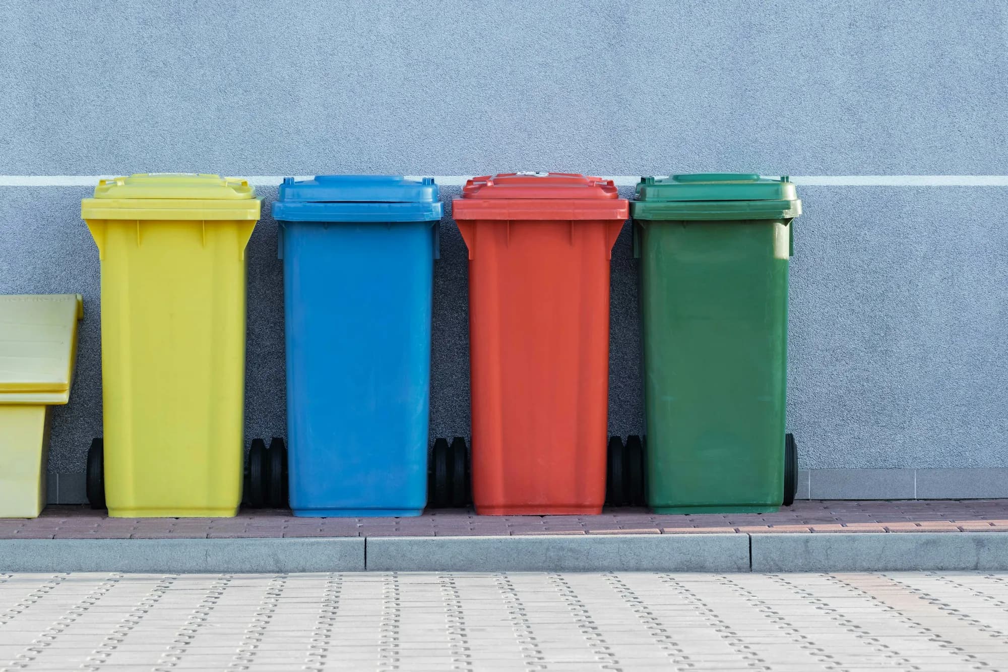 Yellow, blue, red and green wheelie bins in a row against a grey wall